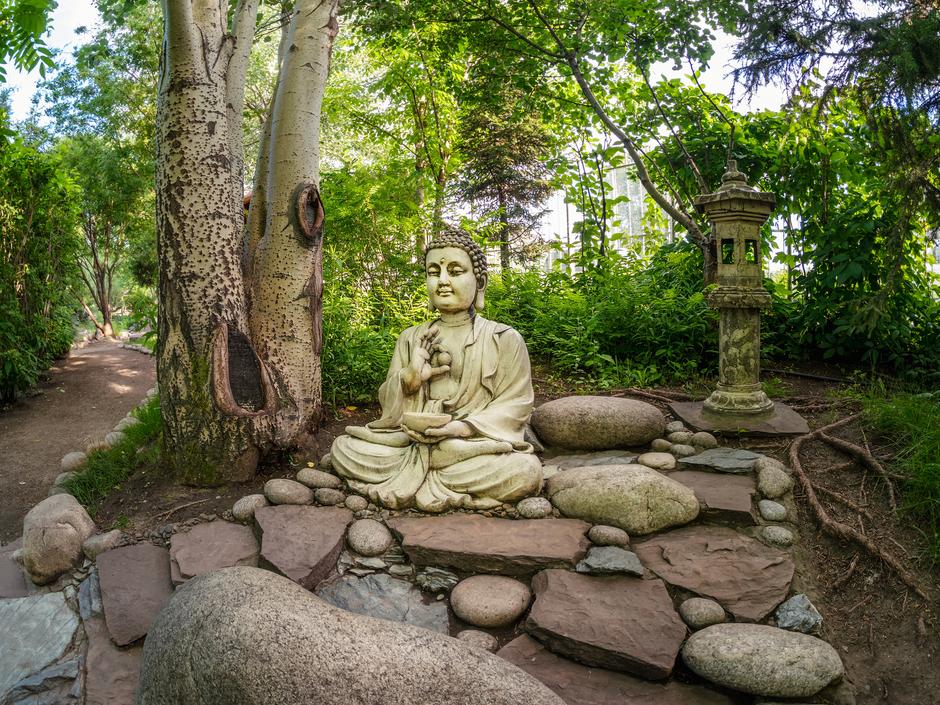 Каменная декоративная статуя Будды в саду под зелеными листьями в городе Абакан